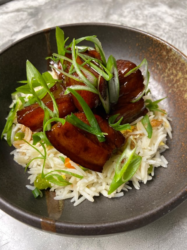 Glazed pork belly with rice and green onions in a ceramic bowl for cocktail reception
